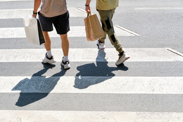 unrecognizable young guys from behind crossing a pedestrian crossing with shopping bags in hand