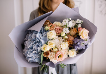 Very nice young woman holding big and beautiful bouquet of fresh hydrangea, roses, eustoma, matthiola, carnations, Delphinium in blue, cream and white colors, cropped photo, bouquet close up