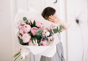 Very nice young woman holding big and beautiful bouquet of fresh peony, matthiola, palm branches and eucalyptus in pink and green colors, cropped photo, bouquet close up