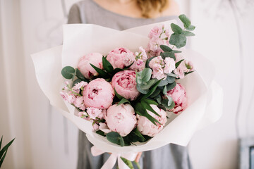 Very nice young woman holding big and beautiful bouquet of fresh peony, matthiola, palm branches and eucalyptus in pink and green colors, cropped photo, bouquet close up