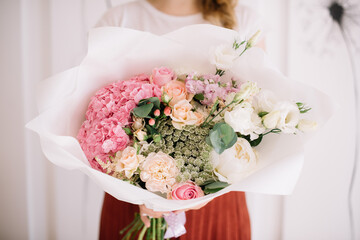 Very nice young woman holding big and beautiful flower bouquet of fresh hydrangea, roses, ammy, carnations, eustoma, peony in white and pink colors