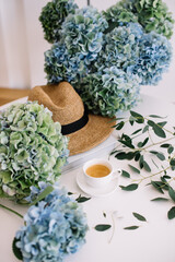 Beautiful blossoming blue hydrangea flowers, beach summer hat, eucalyptus and freshly brewed cup of...