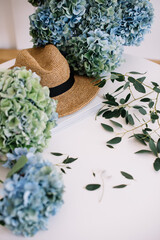 Beautiful blossoming blue hydrangea flowers, beach summer hat, eucalyptus on the white table background, top view, flat lay