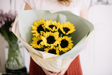 Very nice young woman holding big and beautiful mono bouquet of fresh sunflowers in colors, cropped photo, bouquet close up