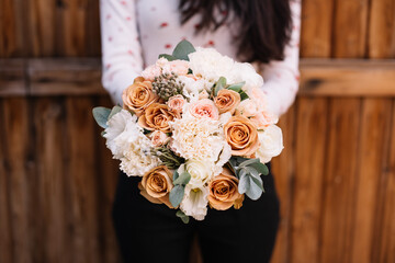 Very nice young woman holding big and beautiful round wedding bouquet of fresh roses, carnations, eustoma, eucalyptus, brunia in white and brown colors, cropped photo, bouquet close up
