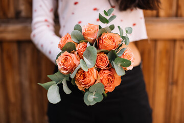 Very nice young woman holding round and beautiful wedding bouquet of fresh orange roses and eucalyptus on the wooden background, cropped photo, bouquet close up - 507767662