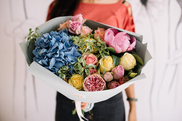 Very nice young woman holding big and beautiful bouquet of fresh hydrangea, roses, peony, carnations in blue, yellow and pink colors, cropped photo, bouquet close up