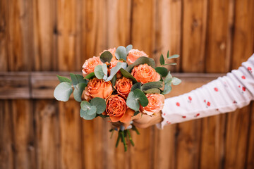 Very nice young woman holding round and beautiful wedding bouquet of fresh orange roses and eucalyptus on the wooden background, cropped photo, bouquet close up - 507767671