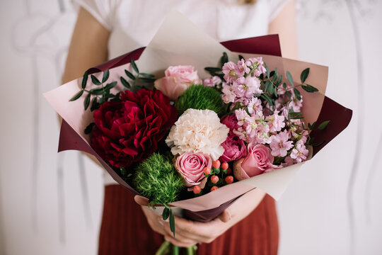 Very nice young woman holding big and beautiful bouquet of fresh peony, roses, carnations, matthiola, pistachio in passionate red and tender purple colors, cropped photo, bouquet close up