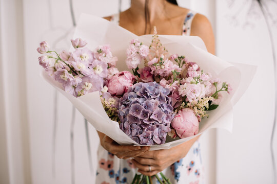 Very nice young woman holding big and beautiful bouquet of fresh delphinium, hydrangea, peony, matthiola in pastel pink and purple colors, cropped photo, bouquet close up