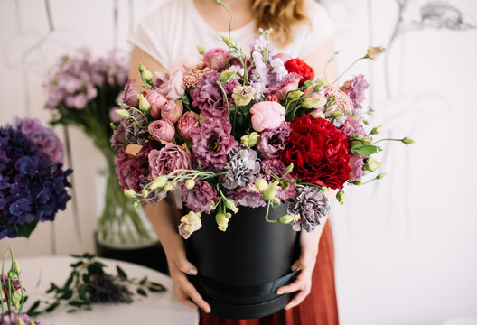 Very nice young woman holding big and beautiful floral composition of fresh peony, roses, carnations, eustoma, matthiola in purple and red colors, cropped photo, bouquet close up