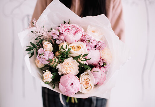 Very nice young woman holding big and beautiful bouquet of fresh peonies, roses, pistachio, carnations, matthiola in pink and cream colors, cropped photo, bouquet close up