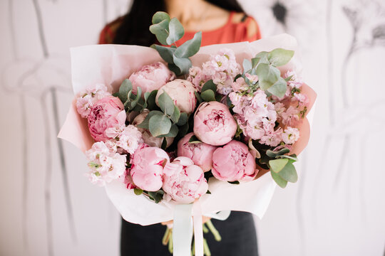 Very nice young woman holding big and beautiful bouquet of fresh peony, matthiola and eucalyptus in tender pink colors, cropped photo, bouquet close up