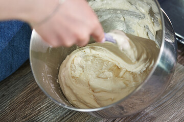 female hand kneading dough for biscuit in a large metal bowl