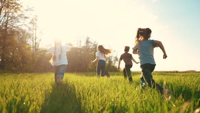 kids run in the park. a large group of a team of children running back view sunlight in the summer on the grass in the park camera lifestyle movement. people in the park happy family kid dream concept