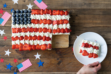 Square cake with the colors of the US flag on a wooden background with decoration. Hand with plate...