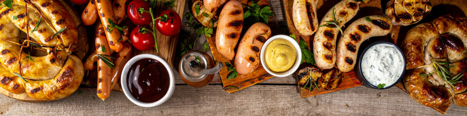 Fototapeta Mix bar-b-q sausages - bavarian, round, gumberland, bratwurst with ketchup, mustard barbeque sauce. Various bbq grilled sausages flat lay on wood background. Street festival grill food menu. obraz