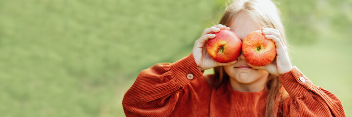 portrait of girl eating red organic apple outdoor. Harvest Concept. Child picking apples on farm in autumn. Children and Ecology. Healthy nutrition Garden Food. Girl holding in front of her face apple