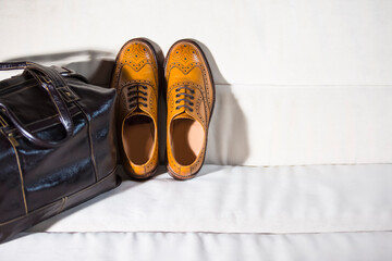 Fashion Footwear Ideas. Male Tanned Full Broggued Oxford Calf Leather Shoes Along With Dark Brown Leather Business Bag on Pale Sofa. - obrazy, fototapety, plakaty
