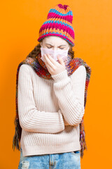 Healthcare Ideas.Teenage Female Girl in Warm Knitted Hat and Scarf Using Facial Mask Against Viruses While Coughing Over Trendy Yellow Background.