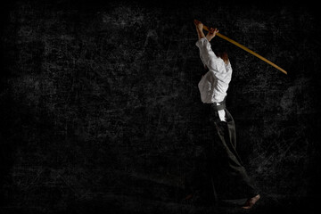 A girl in black hakama standing in fighting pose with wooden sword bokken over black background....