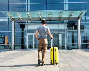 rear view of young man traveler in casual clothes carrying a yellow suitcase next to the entrance...