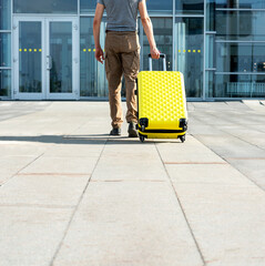 rear view of young man traveler in casual clothes carrying a yellow suitcase next to the entrance...