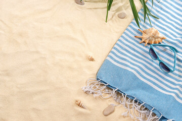 Top view of striped blue towel with sunglasses on sandy beach. Background with copy space and visible sand texture.