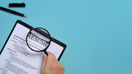 Man holding a magnifying glass over resumes of applicants. Job search concept