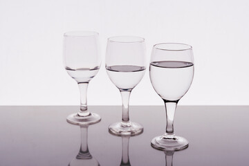 Three wine glasses filled with water reflected on the table