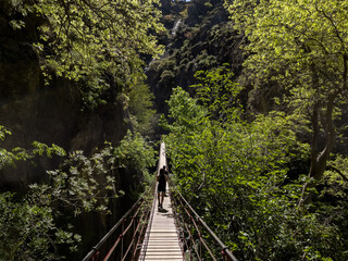 Backpackers crossing a suspension bridge while hiking in the mountains. Travel, active lifestyle and adventure concept.