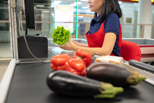 Asian Woman Wearing Red Apron Sitting At Cash Desk Beeping Vegetables