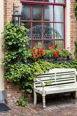 A bench in front if a old farmhouse with plants and roses and a window.