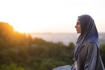 Portrait beautiful young girl in a hijab meditates and practices yoga on a background of sunset and...