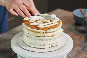 female hands level the cream with a spatula and cover the round cake with butter cream. making a homemade cake. DIY baking