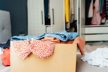 A cardboard box of selected clothes for donating to a Charity shop standing on the bed....