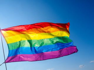 Rainbow flag waving in the wind against clear blue sky