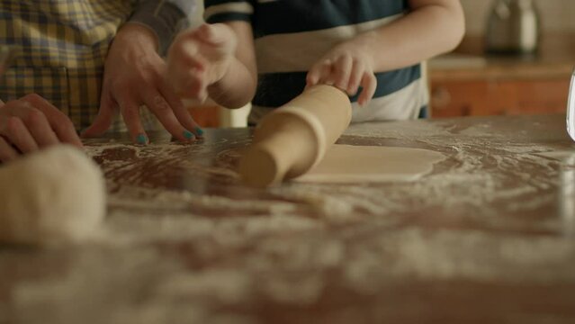 Close up of kid rolling dough standing with his mom in the kitchen. Happy family baking together at home. Handheld camera.
