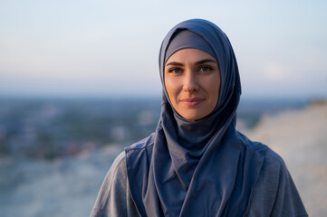 Portrait of a young beautiful girl in a hijab looking at the camera on a background of sunset and landscape
