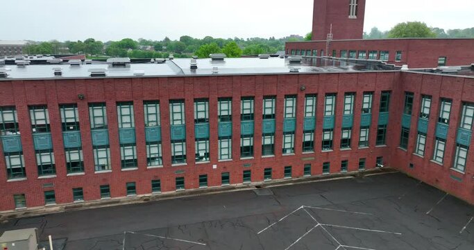Aerial pan of high school building. Brick school with many classrooms and windows. Exterior view on wet and rainy spring day.