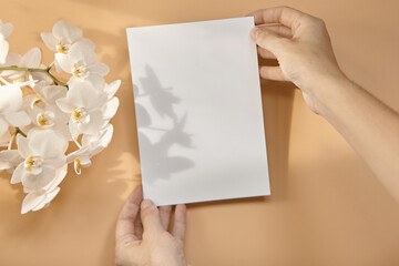Obraz premium Hands are holding an empty white A5 form on a beige background.