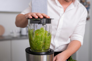 Unrecognizable man making green homemade smoothie in blender. Healthy lifestyle concept.