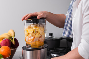 Close up cropped shot of man making smoothie from fresh fruits in professional blender or food...