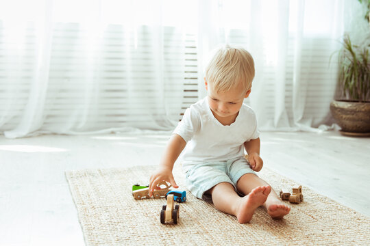 Child boy playing with wooden cars toys, sitting on the floor, while staying at home, eco minimalism design