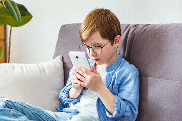Child boy in glasses plays tablet. Astigmatism, myopia, strabismus, poor vision concept