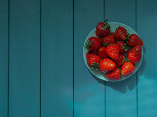 Strawberries on a white saucer on a wooden background from wooden planks