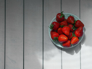 Strawberries on a white saucer on a wooden background from wooden planks
