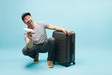 portrait of man with travel suitcase and paper airplane, isolated on blue . Concept of traveling funny and happy emotion tourist.