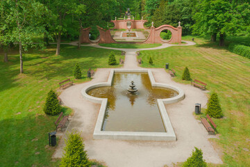Park dworski w mieście Iłowa w zachodniej Polsce. Widać parkową fontannę, alejkę i mur...