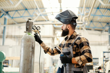 A heavy industry worker preparing welder for welding and unscrew the valve in factory.